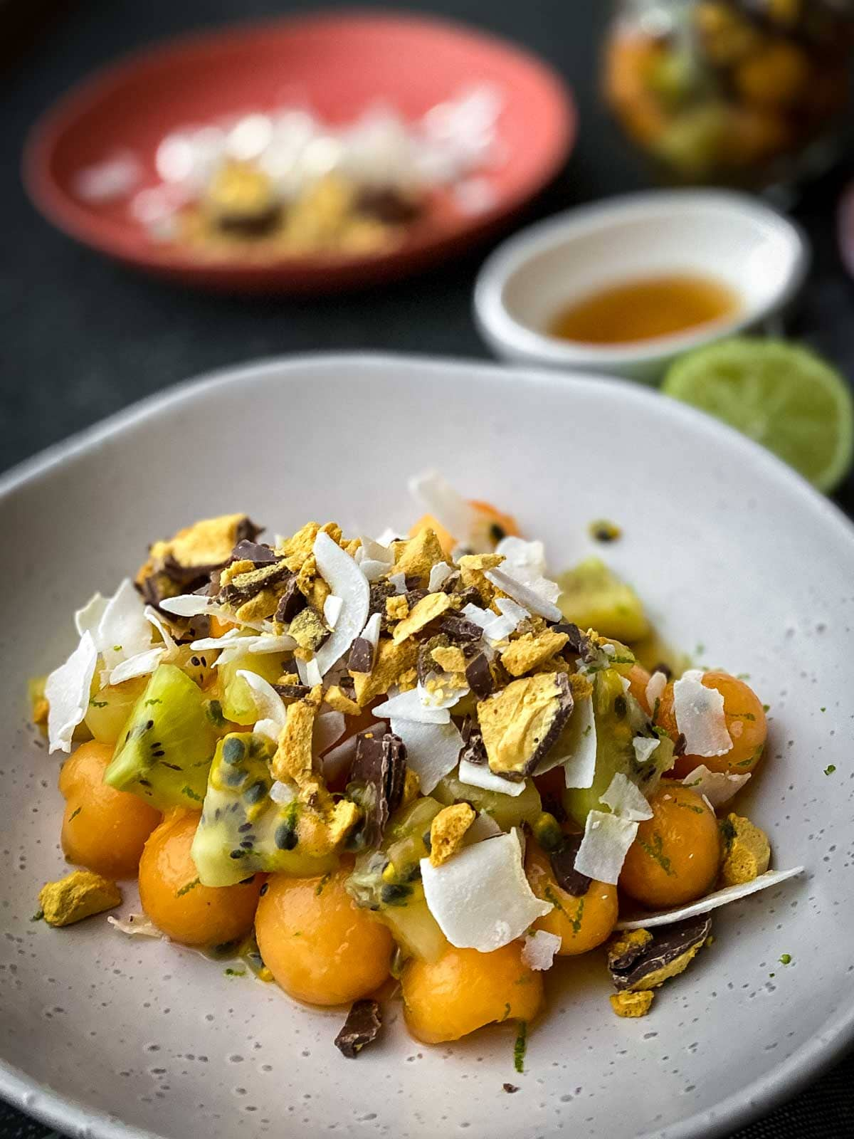 Rockmelon and Passionfruit Salad with Chocolate Honeycomb on a white plate with lime and dressing on the side