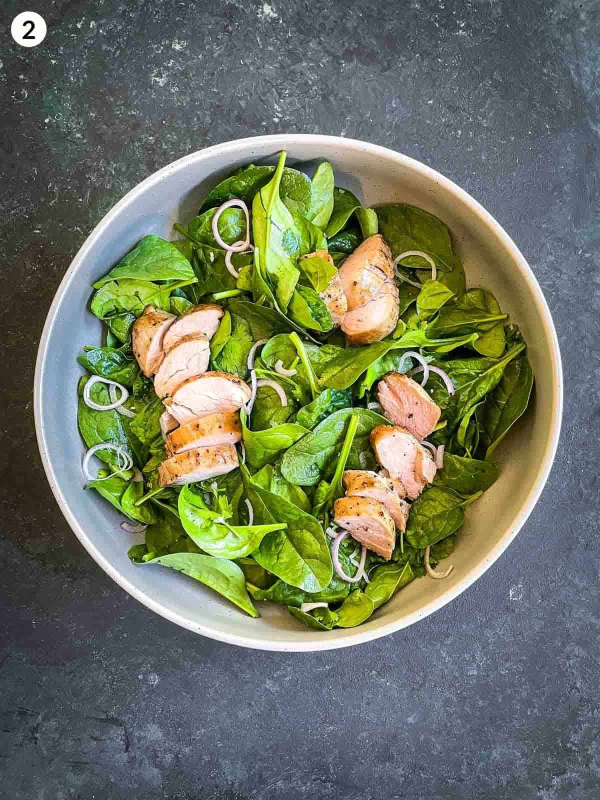 baby spinach leaves, shallots and slices of sous vide pork tenderloin in a round bowl