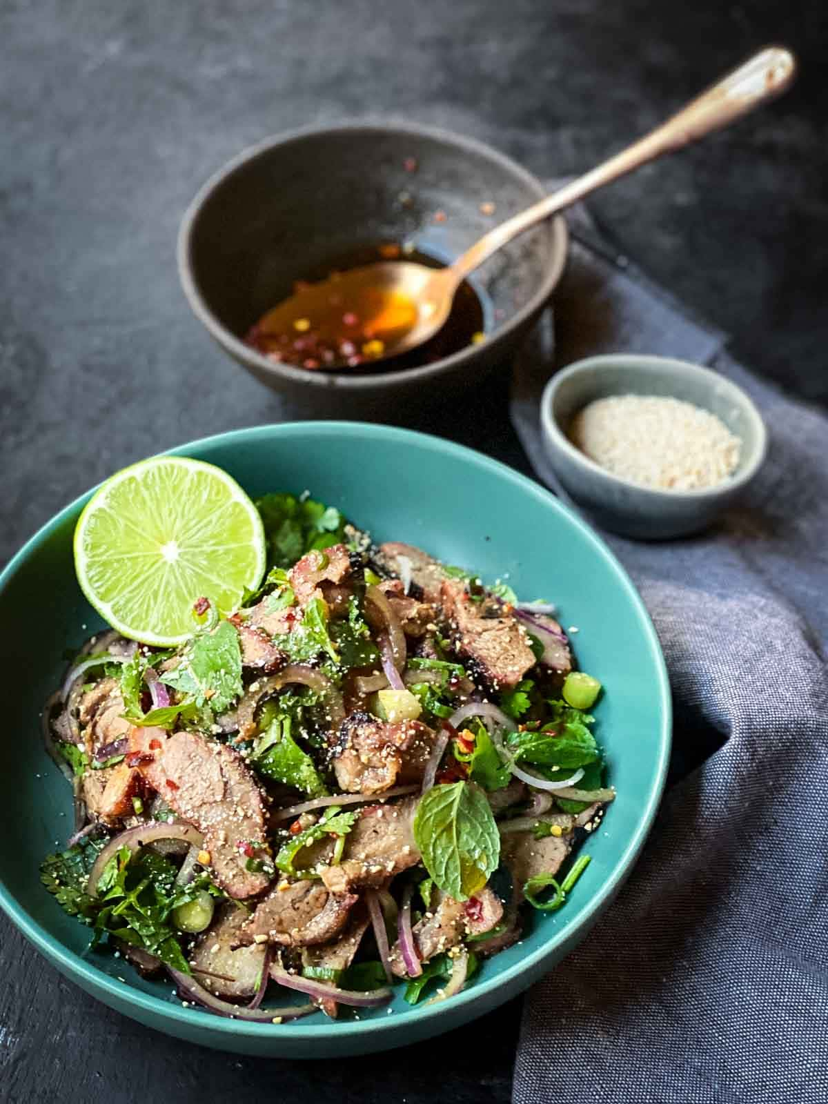 Thai Grilled Pork Salad in a bright blue bowl with half a lime and Thai fish sauce dressing to the side