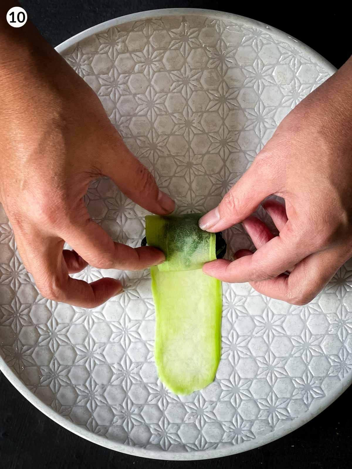 2 hands rolling Chinese squash and spinach rolls on a white plate