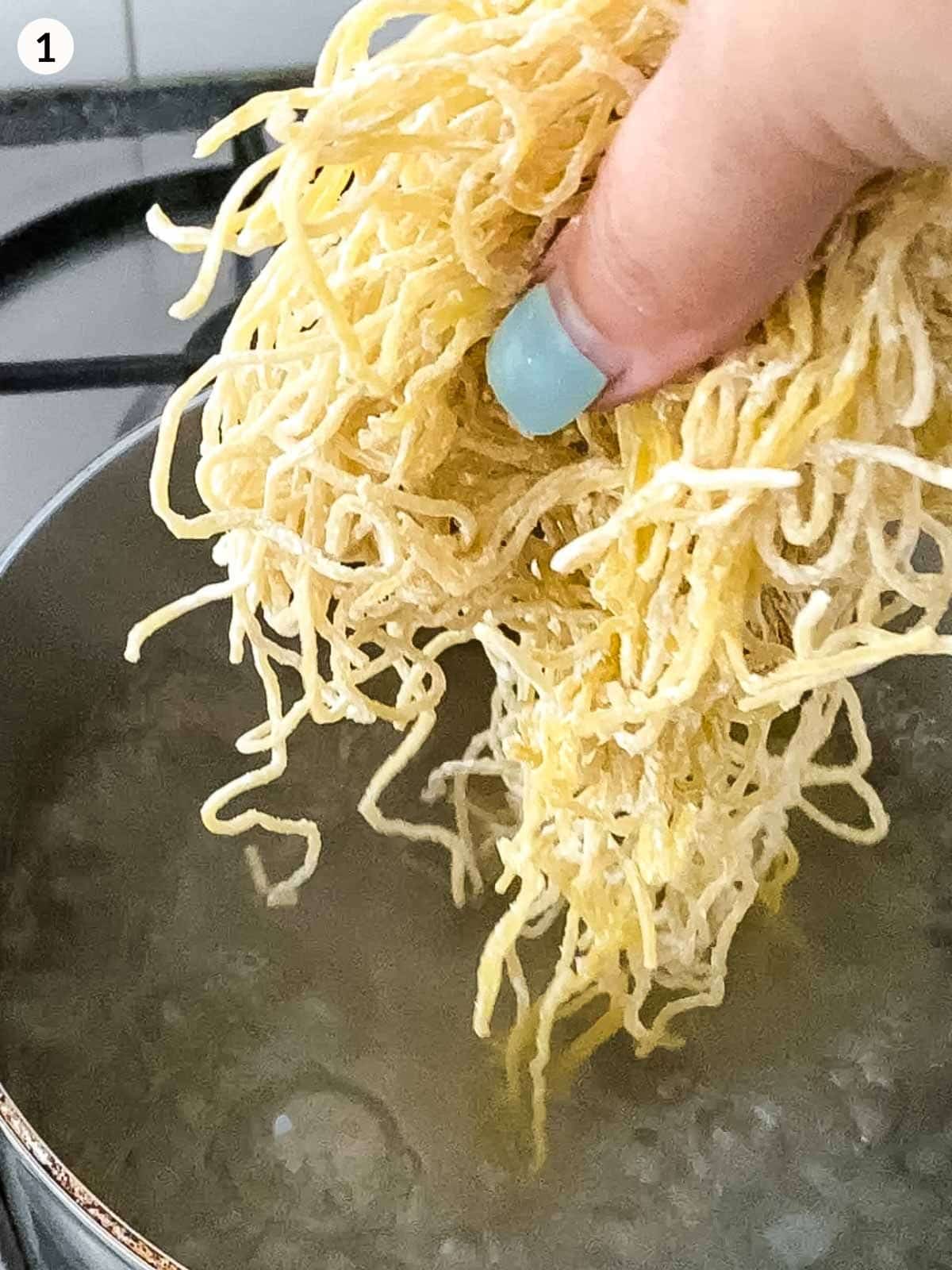 hand holding egg noodles ready to put into pot with boiling water