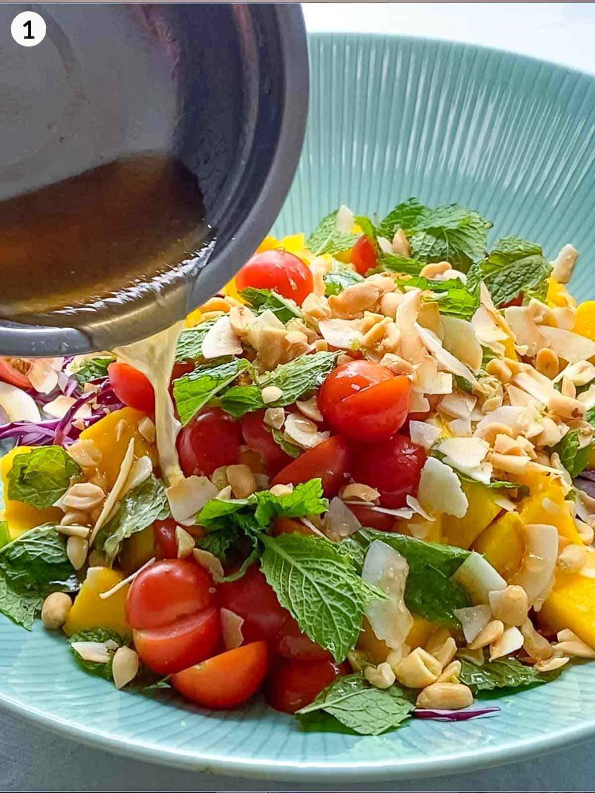 pouring salad dressing into a large green salad bowl with mango salad