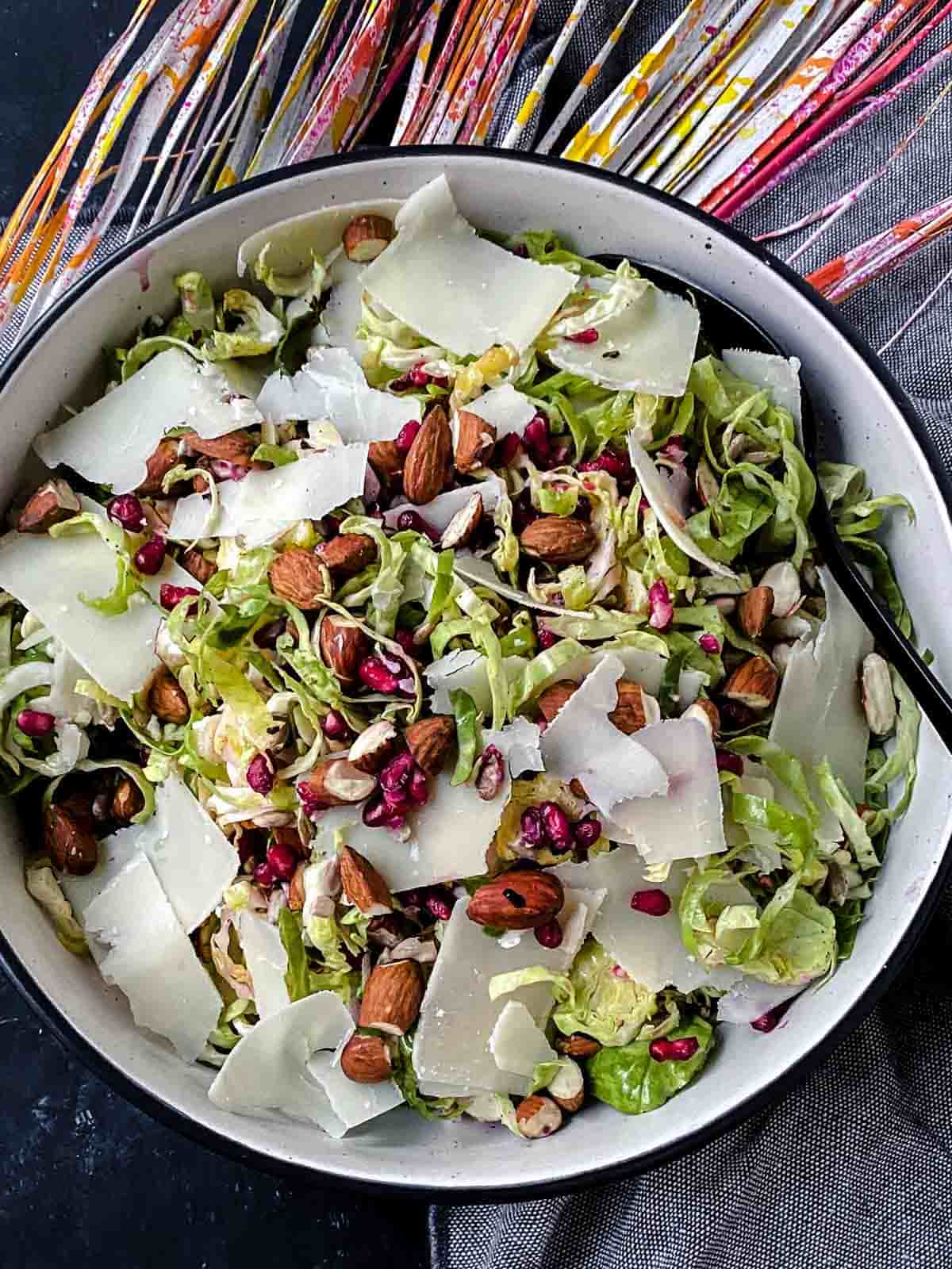 Keto Brussels Sprouts Salad with Shaved Parmesan in a white bowl with colourful fried leaves