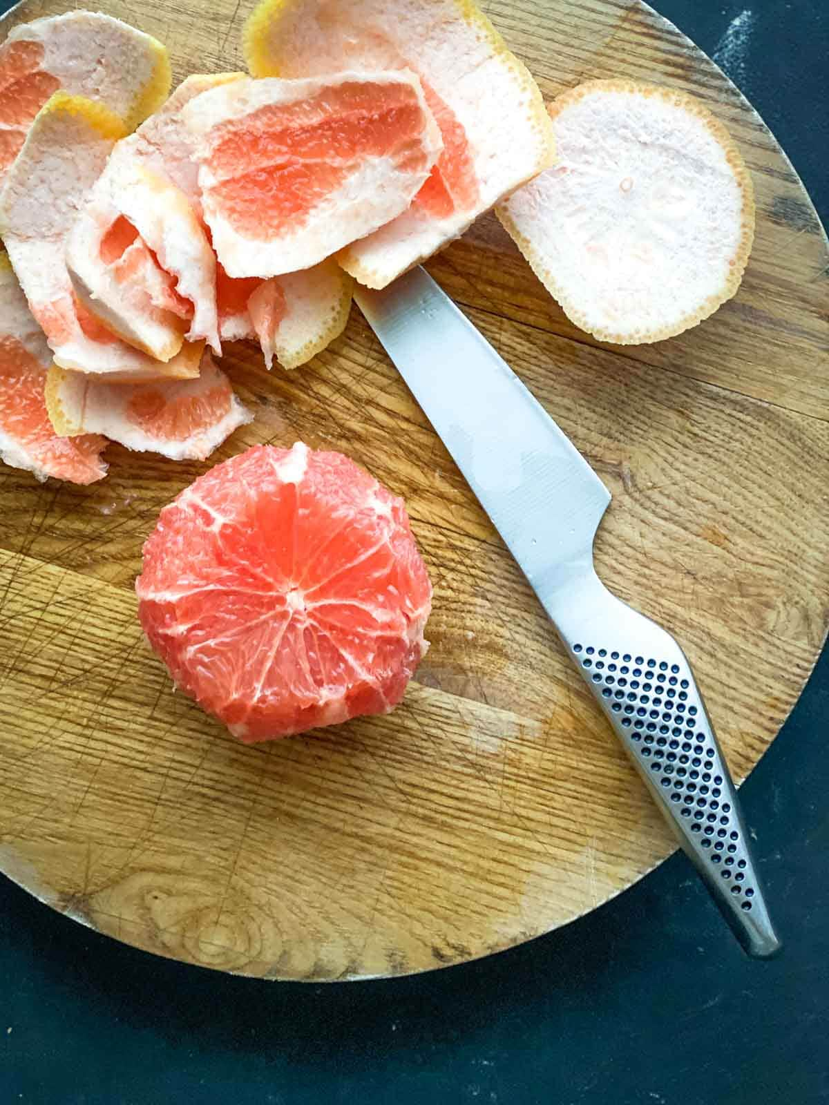 Removing the skin off grapefruit with a knife on a wooden board