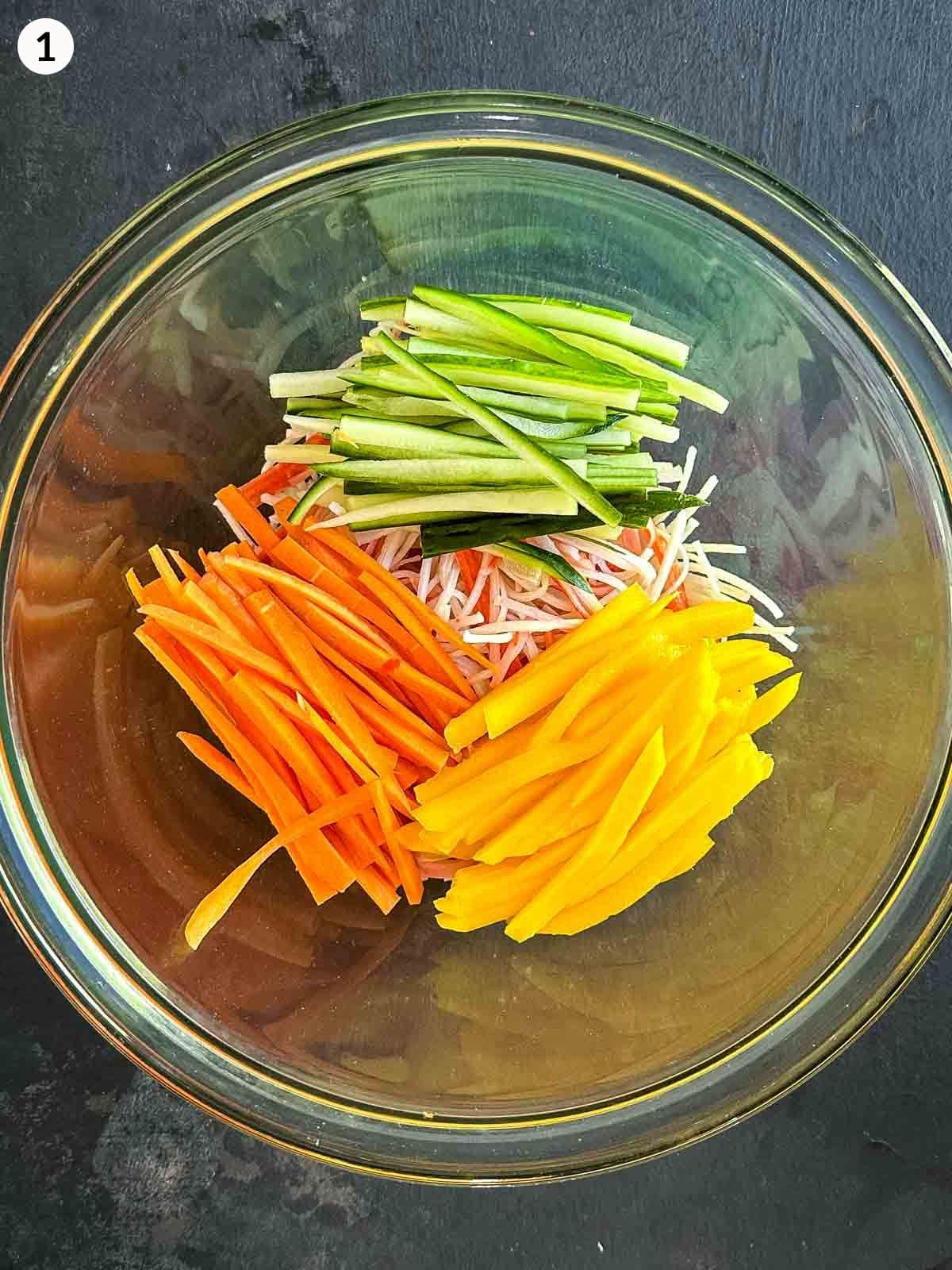 Glass mixing bowl of kani salad ingredients