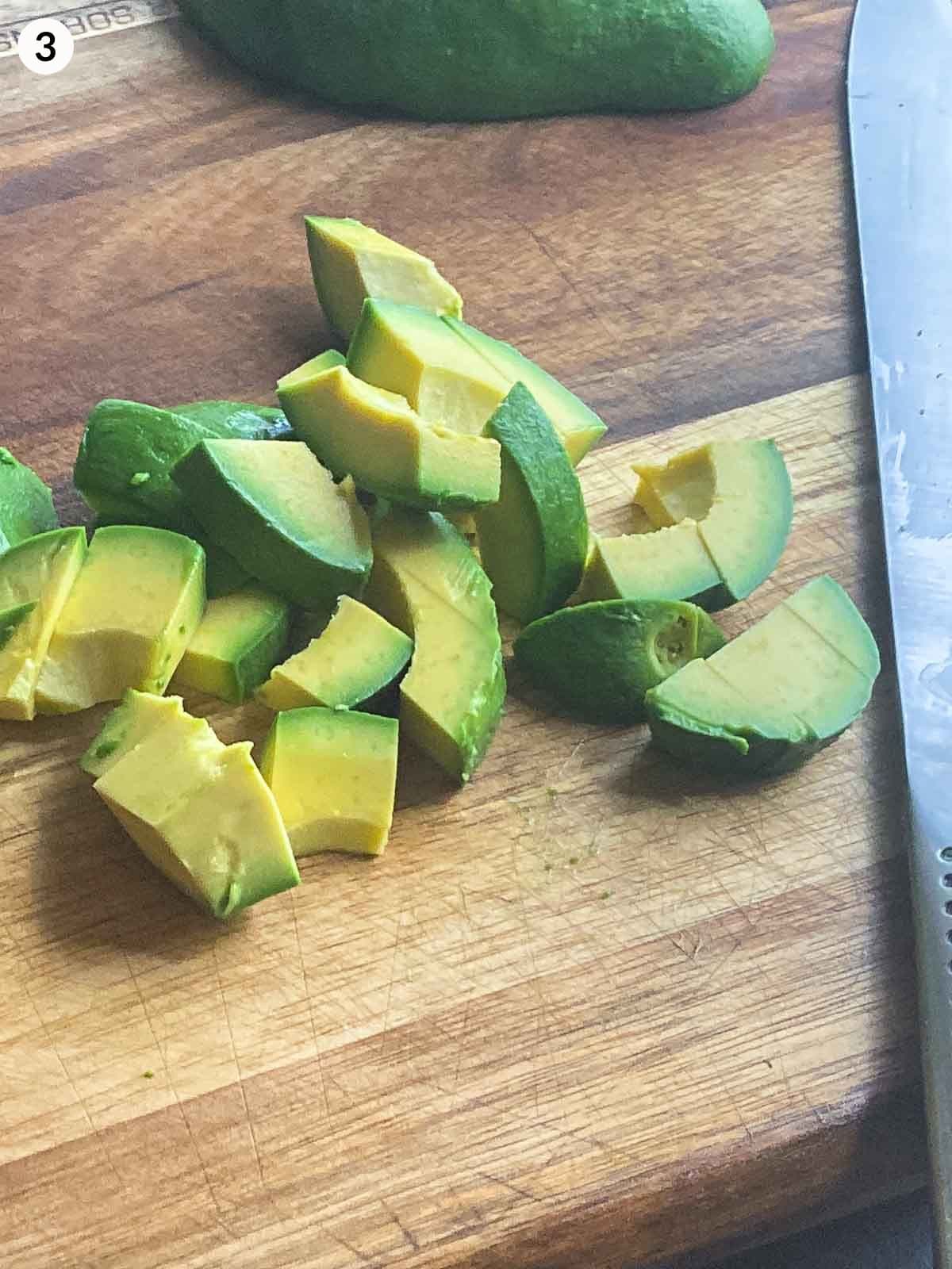 cut avocado on a wooden chopping board with knife next to it