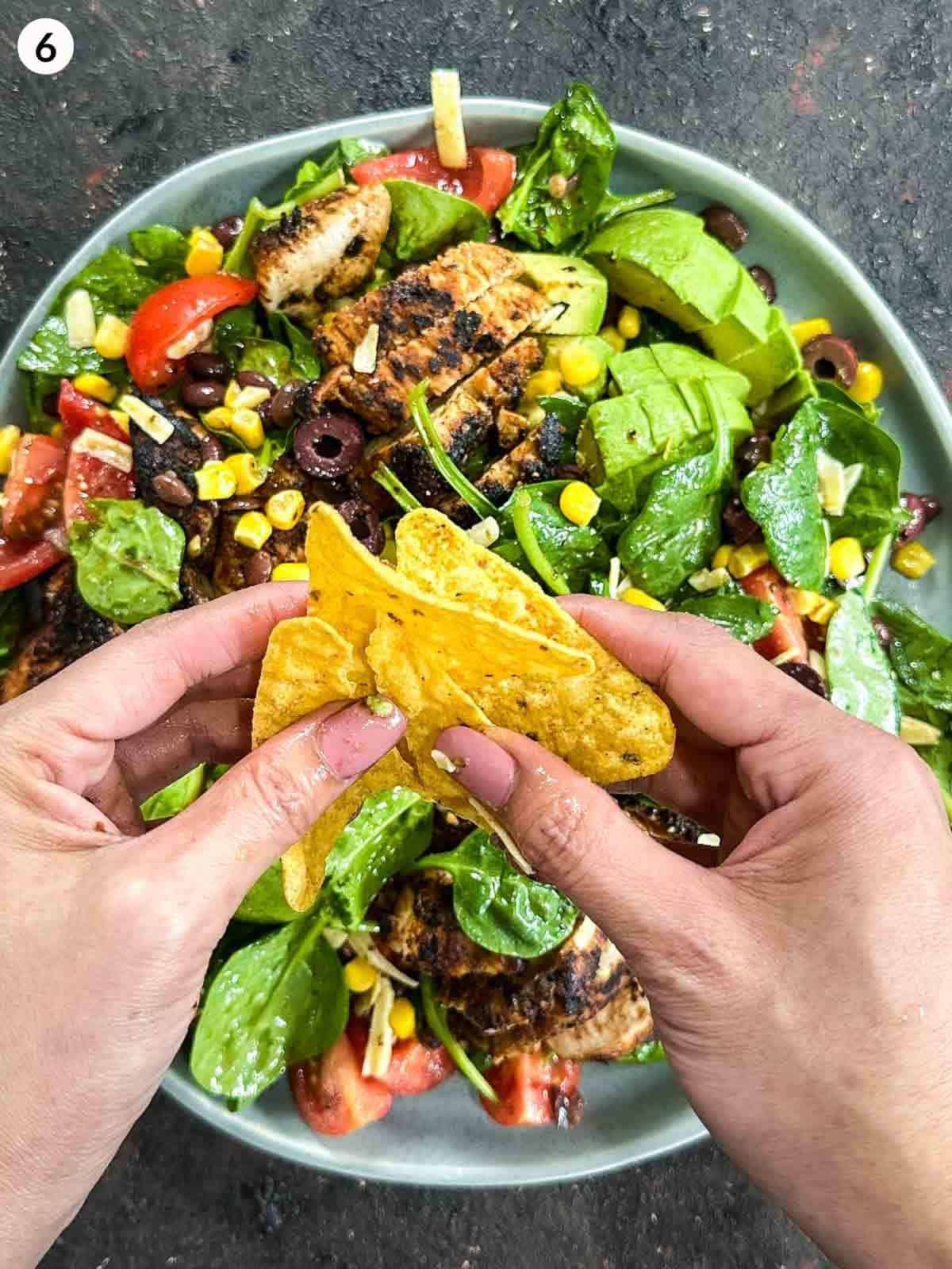 2 hands crushing corn chips over a plate of Santa Fe salad