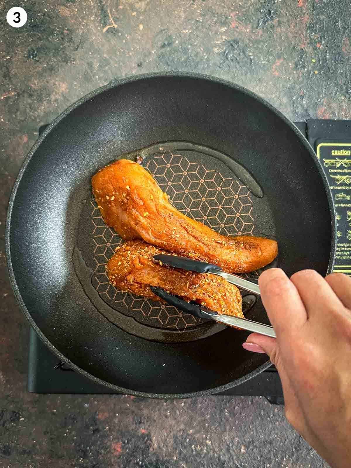 Pan frying chicken tenders in a fry pan with a pair of tongs