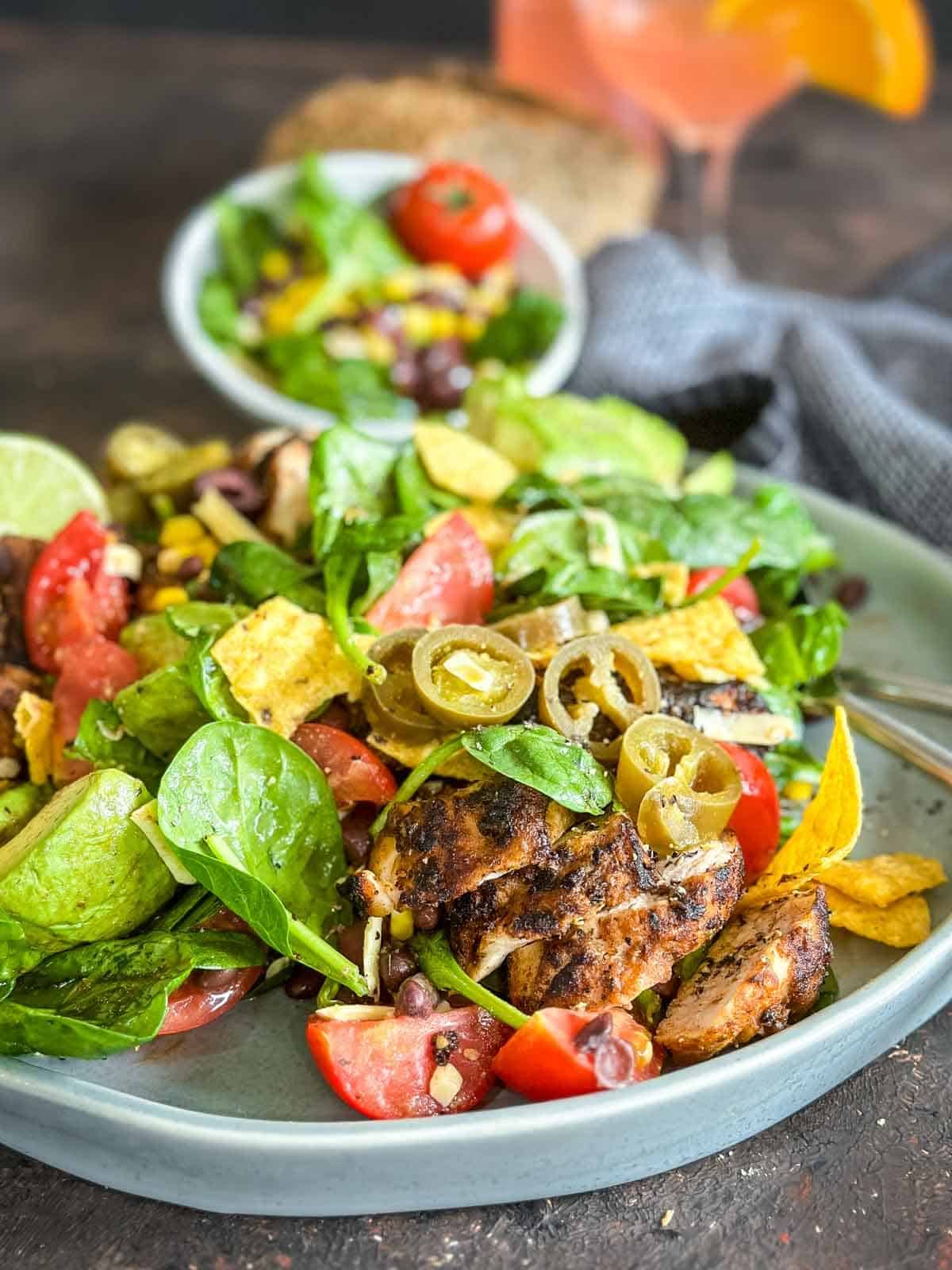 Santa Fe Salad with Chicken on a green plate with salad servers, blue napkin and bread on the side