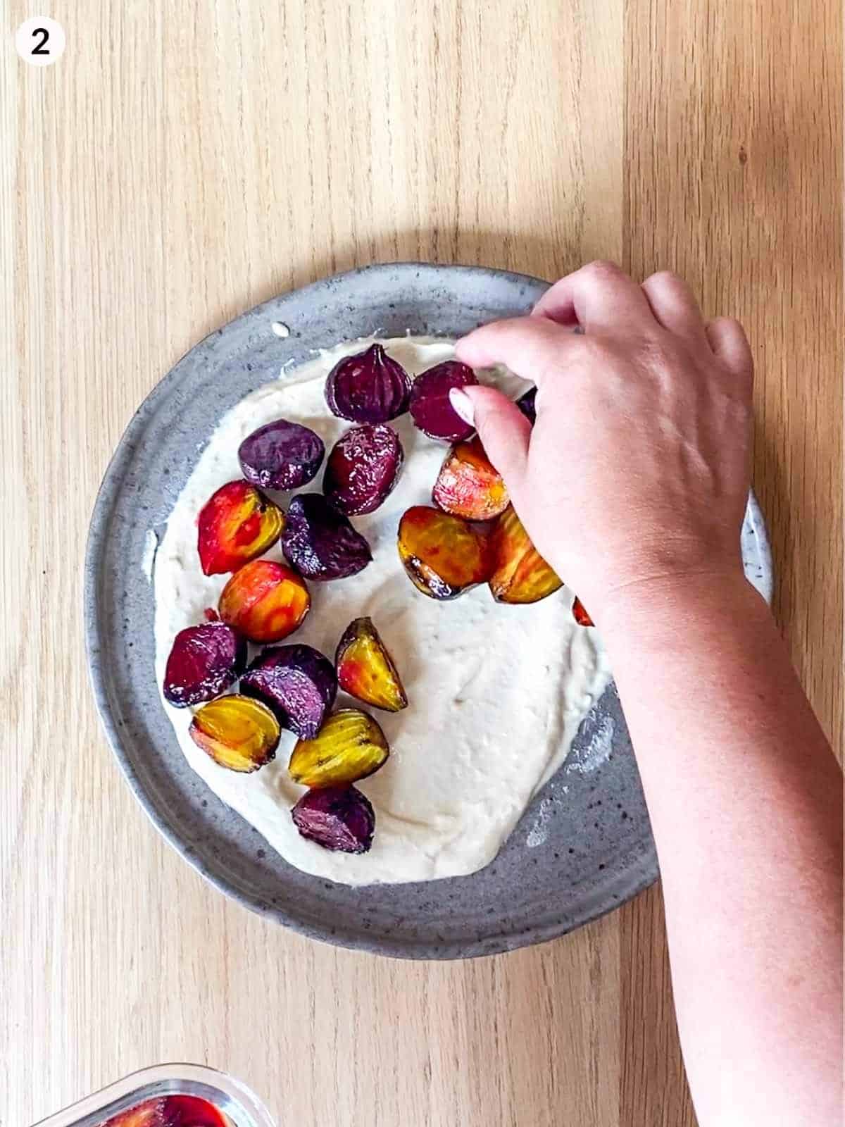 hands adding roasted baby beets on top of hummus on plate