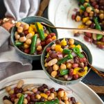 Bowls of 5 bean salad with rose gold spoons, over 2 plates of 5 bean salad