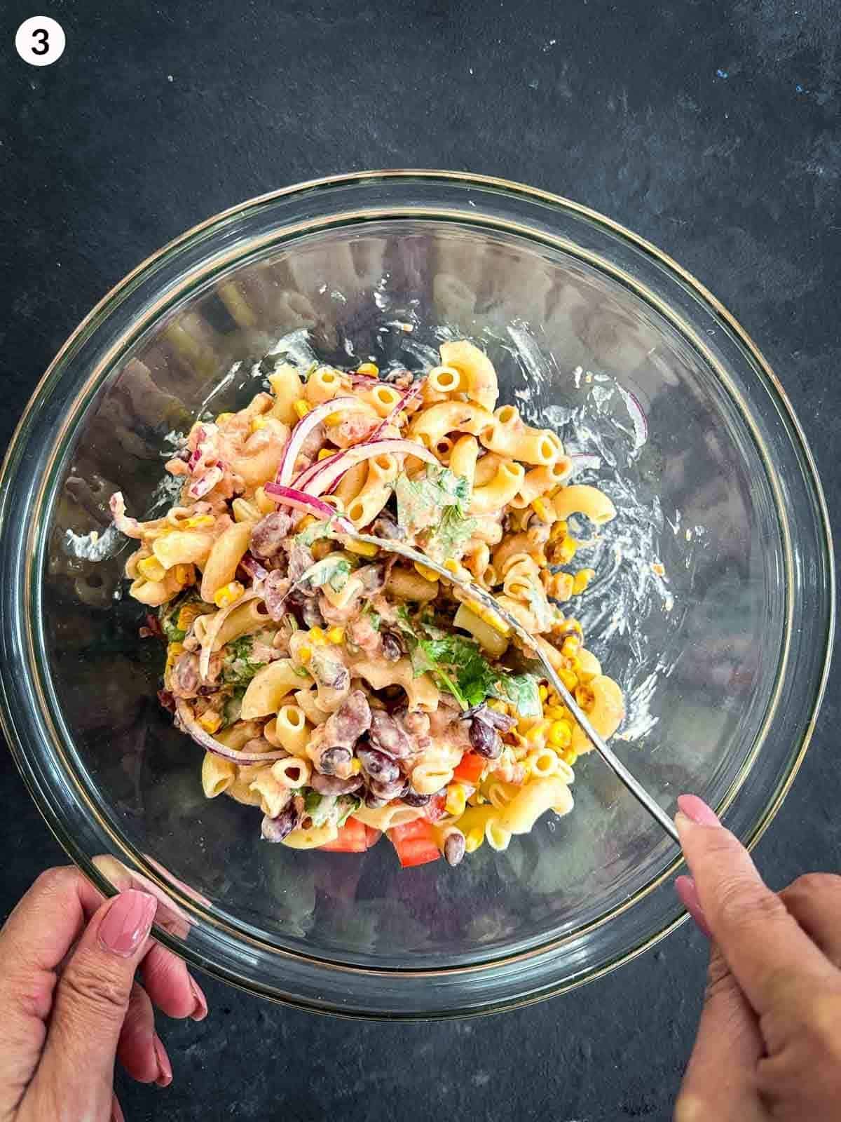 Mixing the ingredients of Mexican Macaroni Salad in a glass bowl