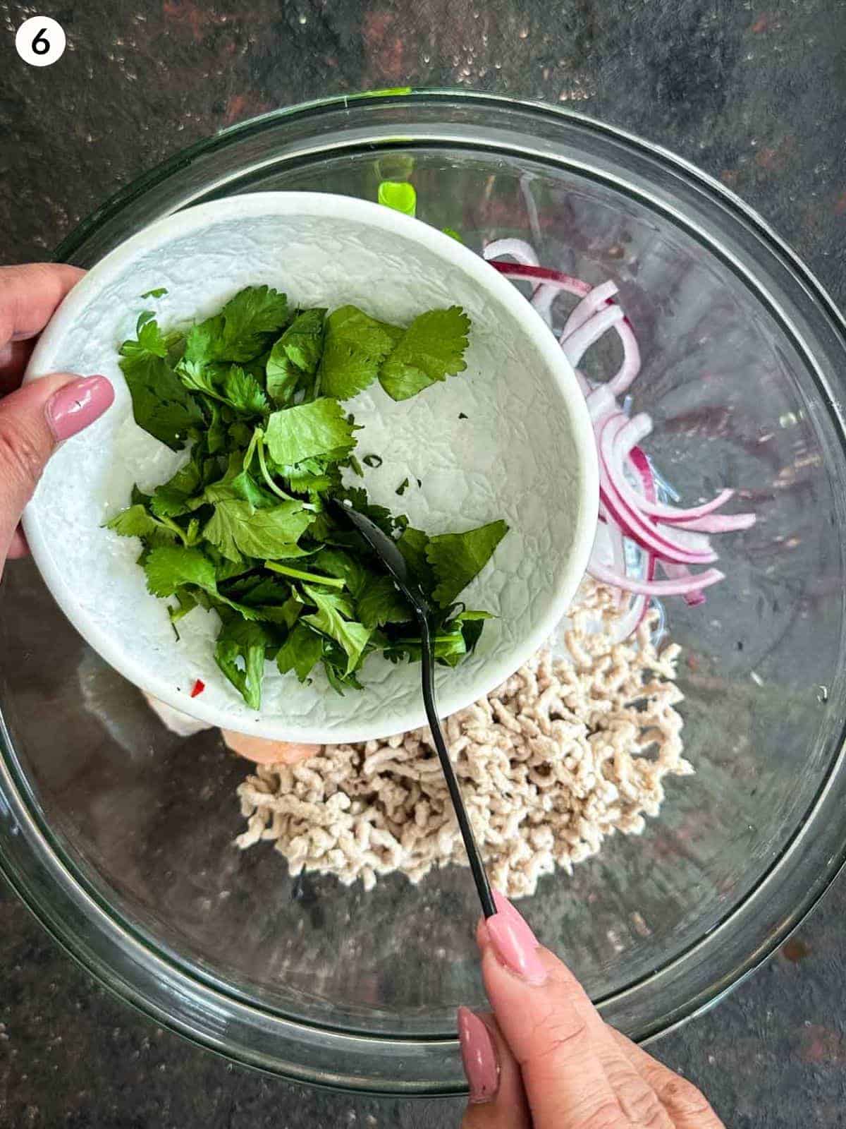 Adding cilantro into a glass bowl of yum woon sen ingredients