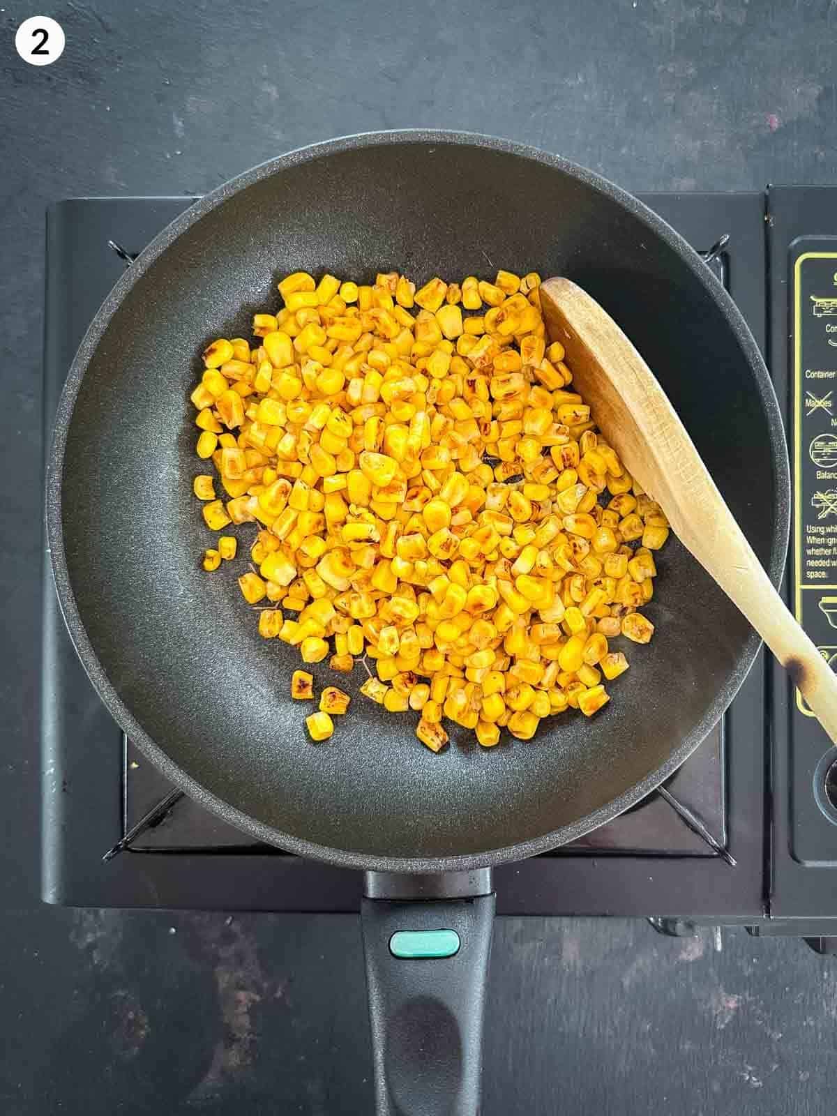 Cooking corn kernels in a fry pan on a stove top with a wooden spoon