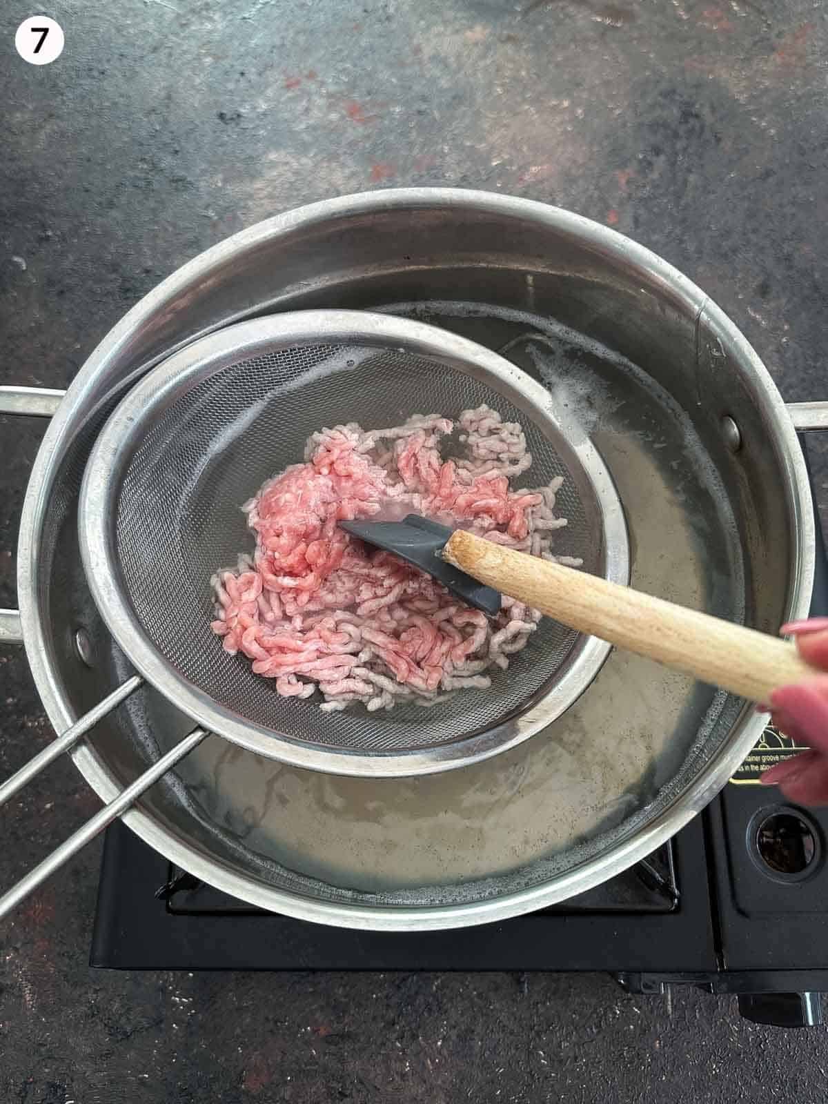 Cooking ground beef in a sieve over a pot of boiling water