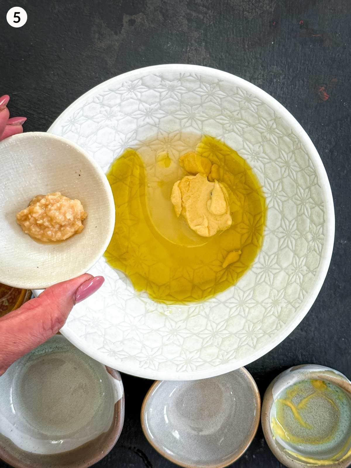 Adding minced garlic into a bowl of olive oil and mustard