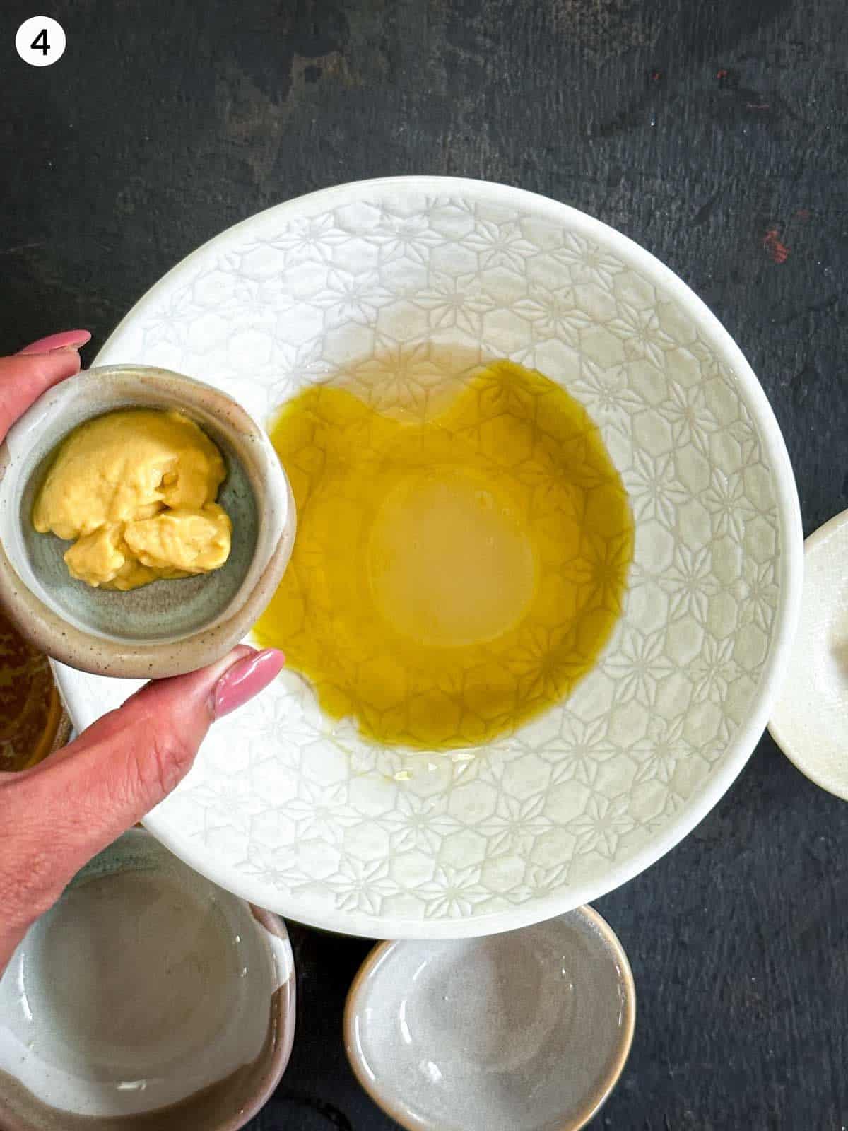 Adding Dijon mustard into a bowl of olive oil and vinegar