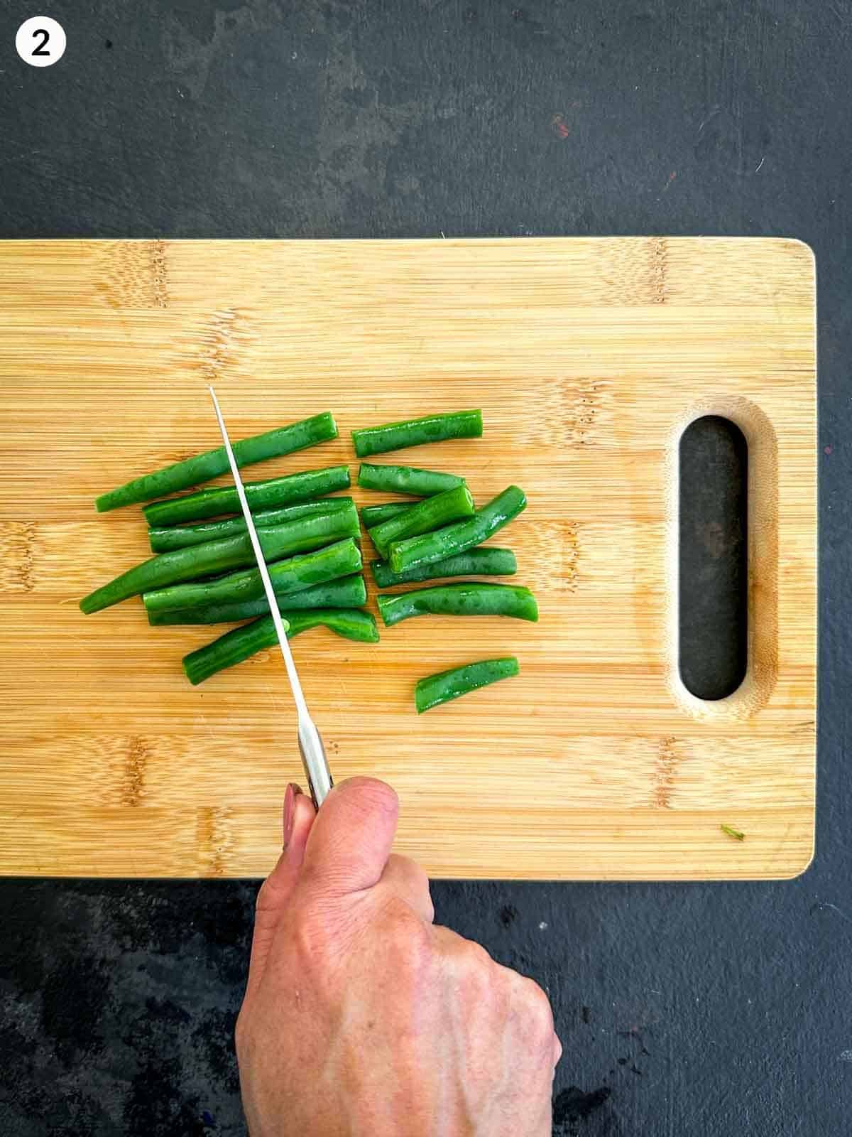 Cutting green beans into 3 with a knife on a wooden chopping board