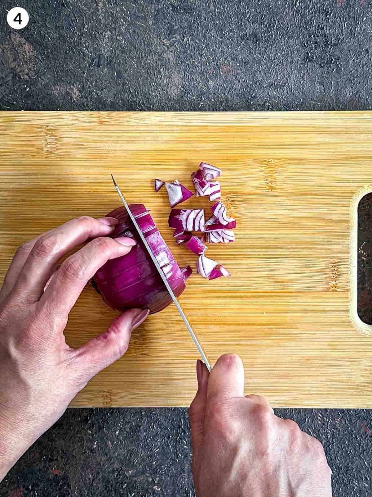 Dicing red onion with a knife on a wooden chopping board