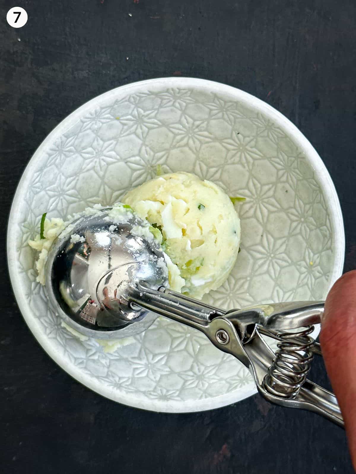 Scooping mashed potato into a white bowl with an ice cream scoop