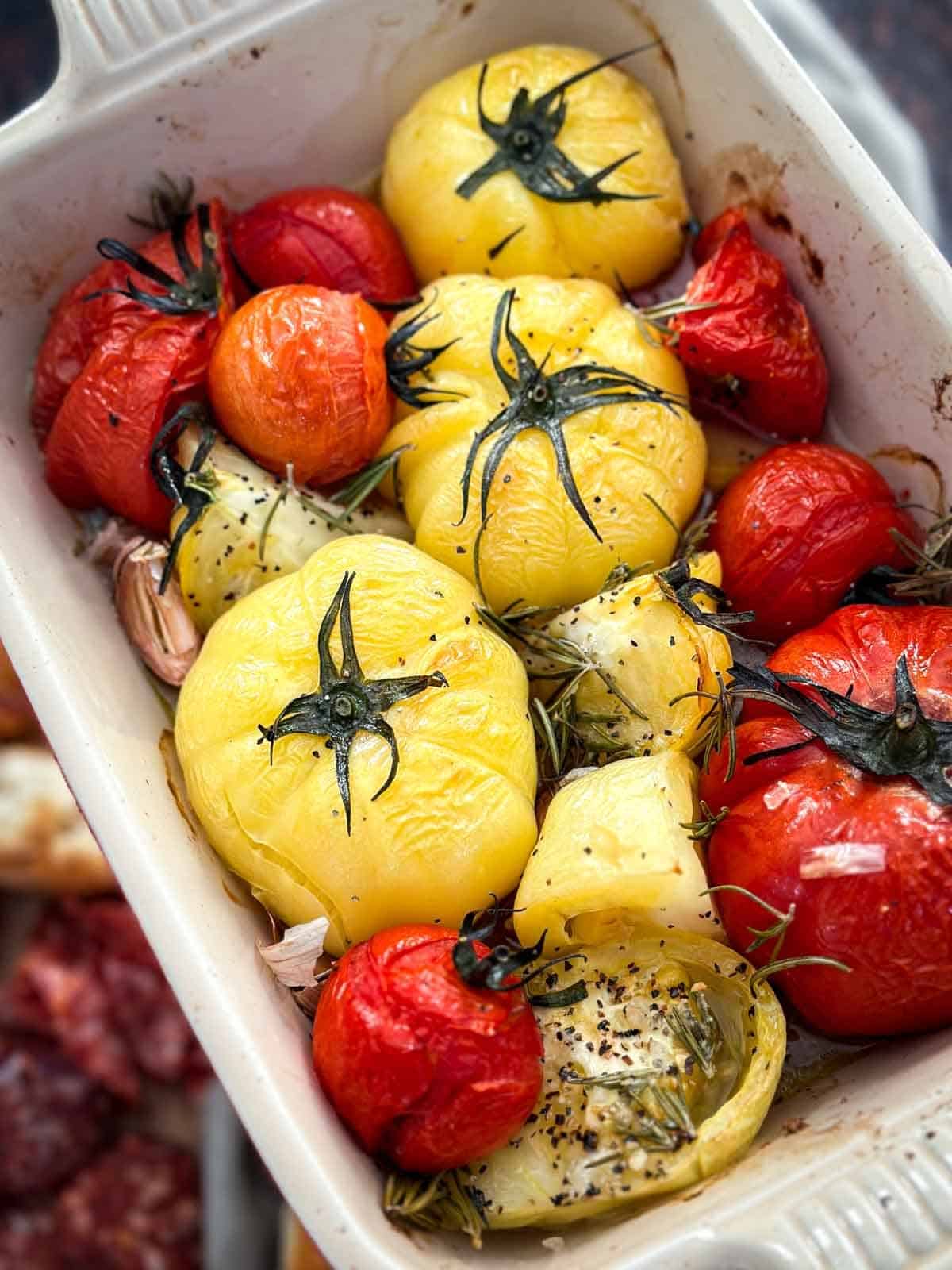 Garlic rosemary roasted beefsteak tomatoes in a baking dish hovering over a charcuterie board