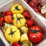 Garlic rosemary roasted beefsteak tomatoes in a baking dish hovering over a charcuterie board