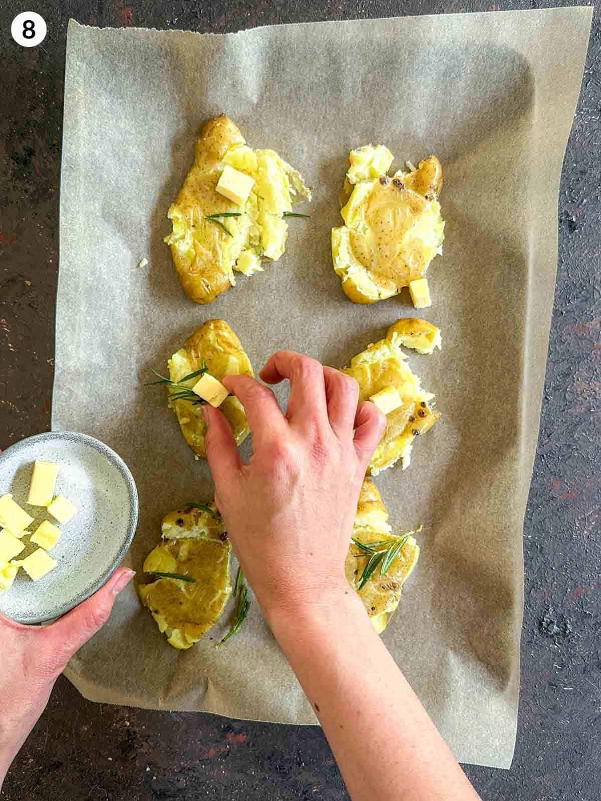 Adding small cubes of butter on top of smashed fingerling potatoes, evenly laid out on parchment paper on a sheet pan