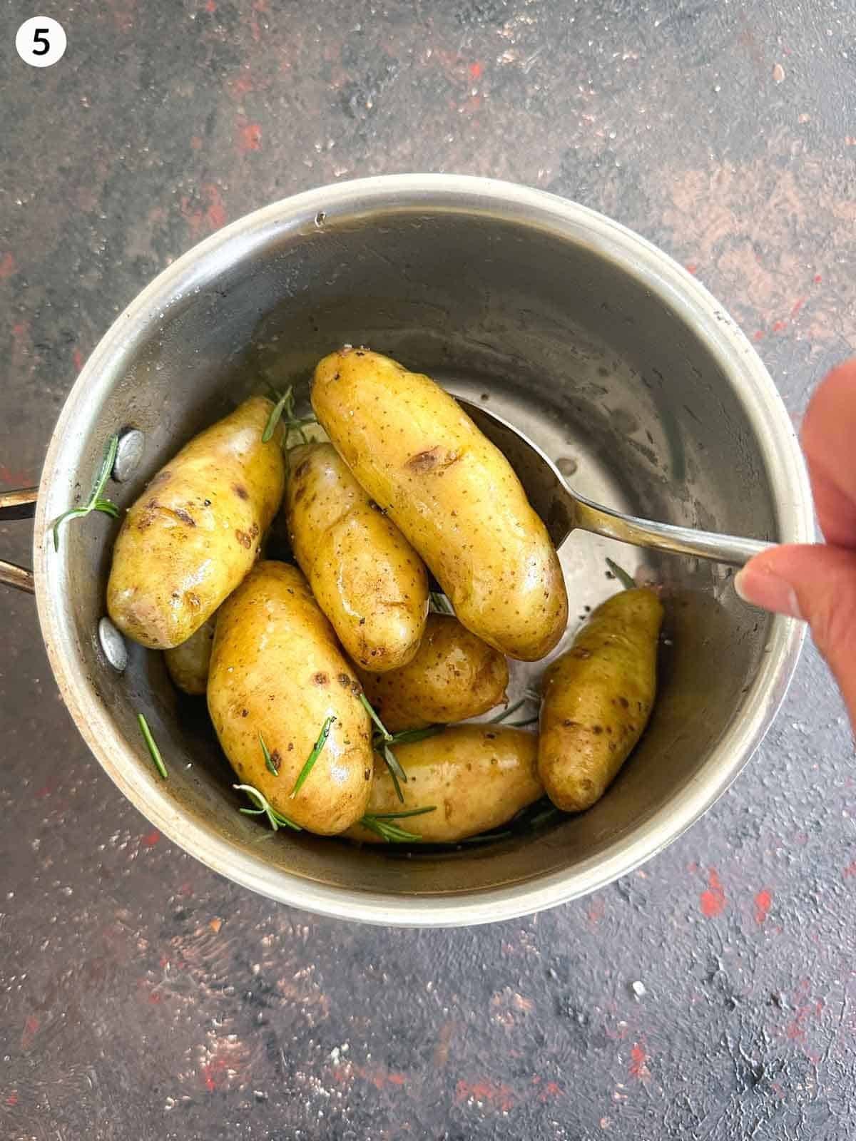 Stirring fingerling potatoes with rosemary and olive oil with a spoon in a pot