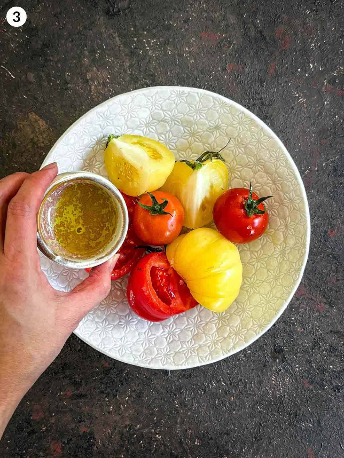 pouring olive oil onto raw beefsteak tomatoes in a white bowl