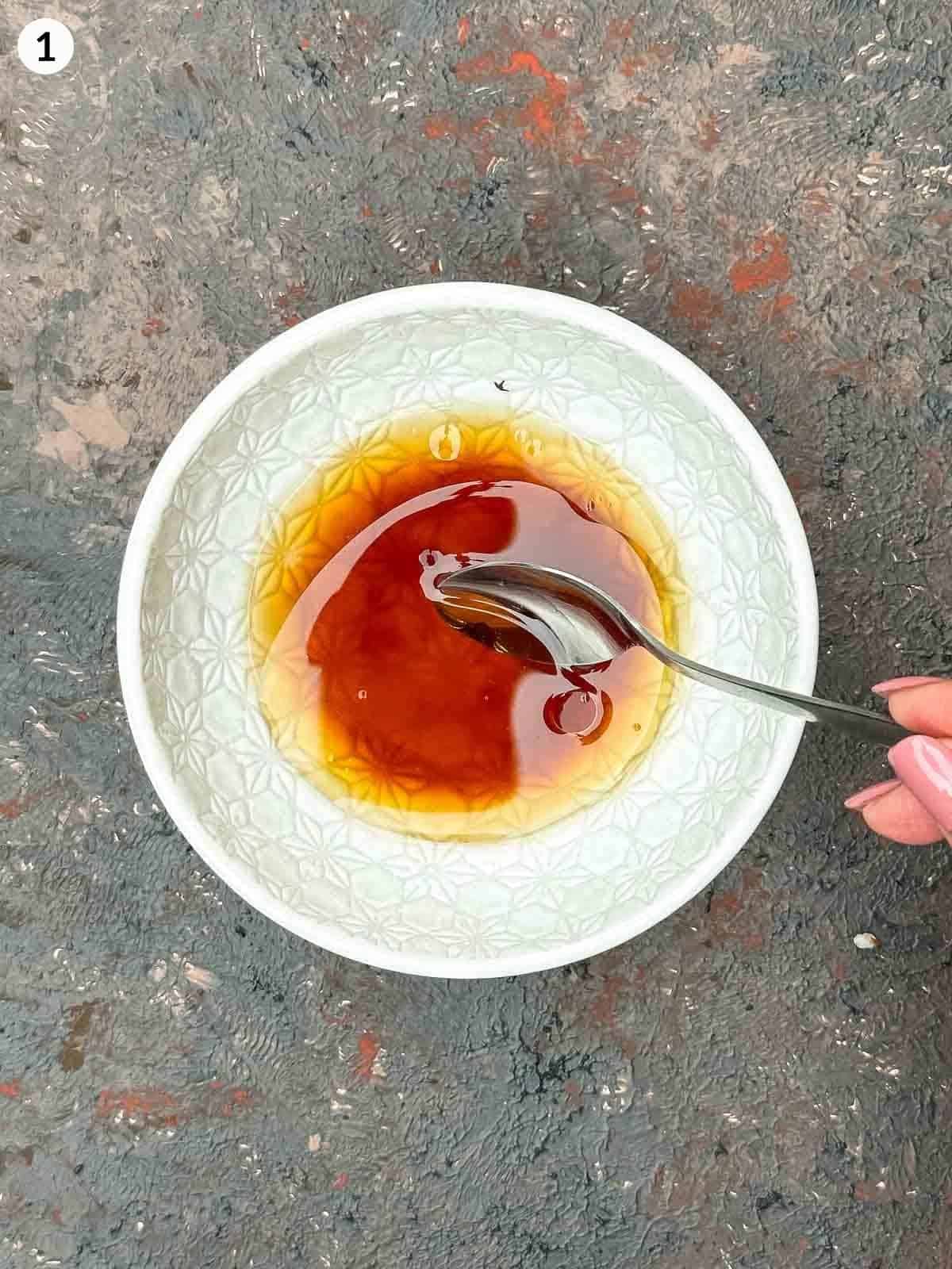 A teaspoon stirring a bowl of sweet soy sesame dressing in a white owl