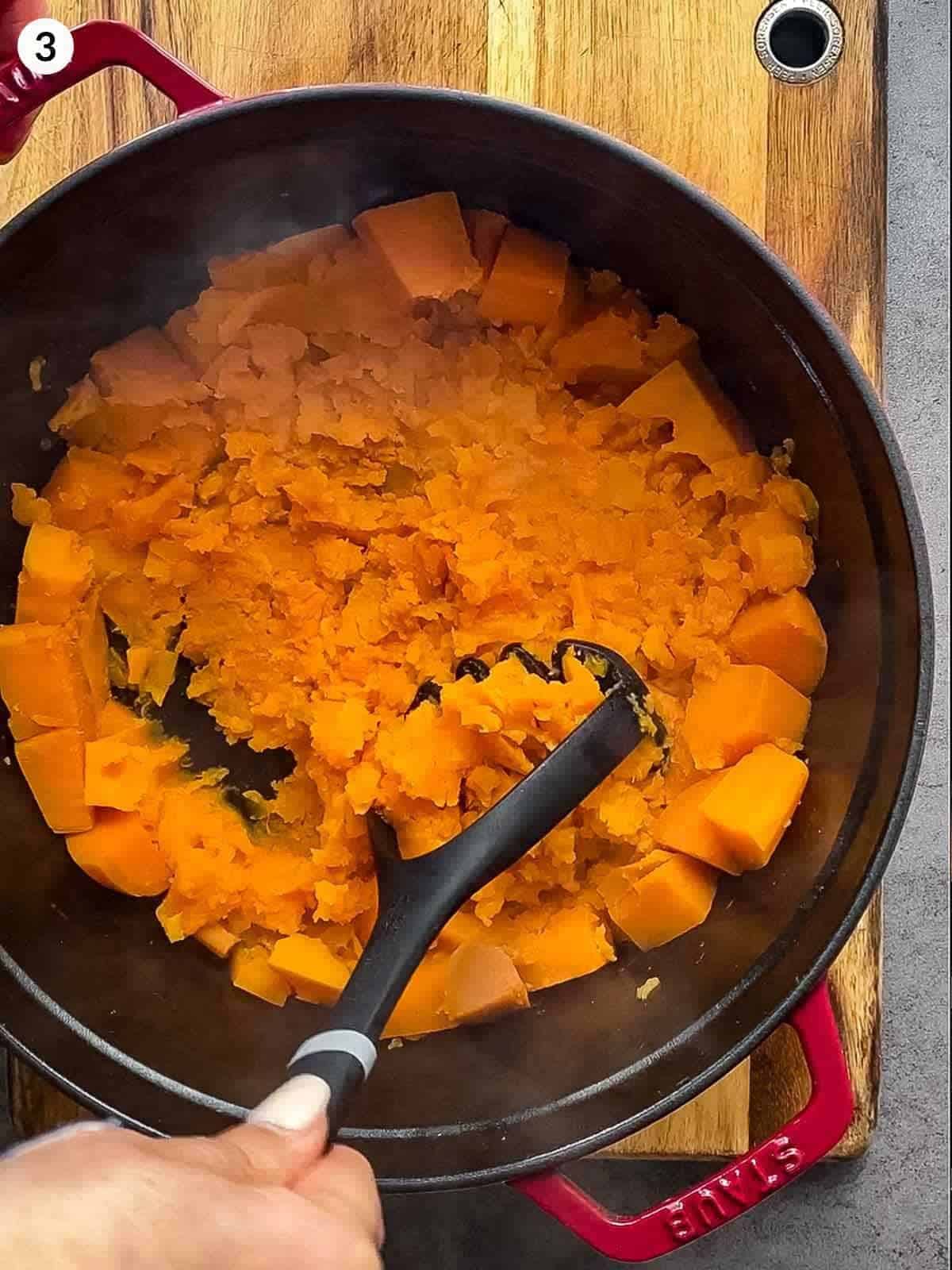 Mashing sweet potato in a Dutch oven with a potato masher