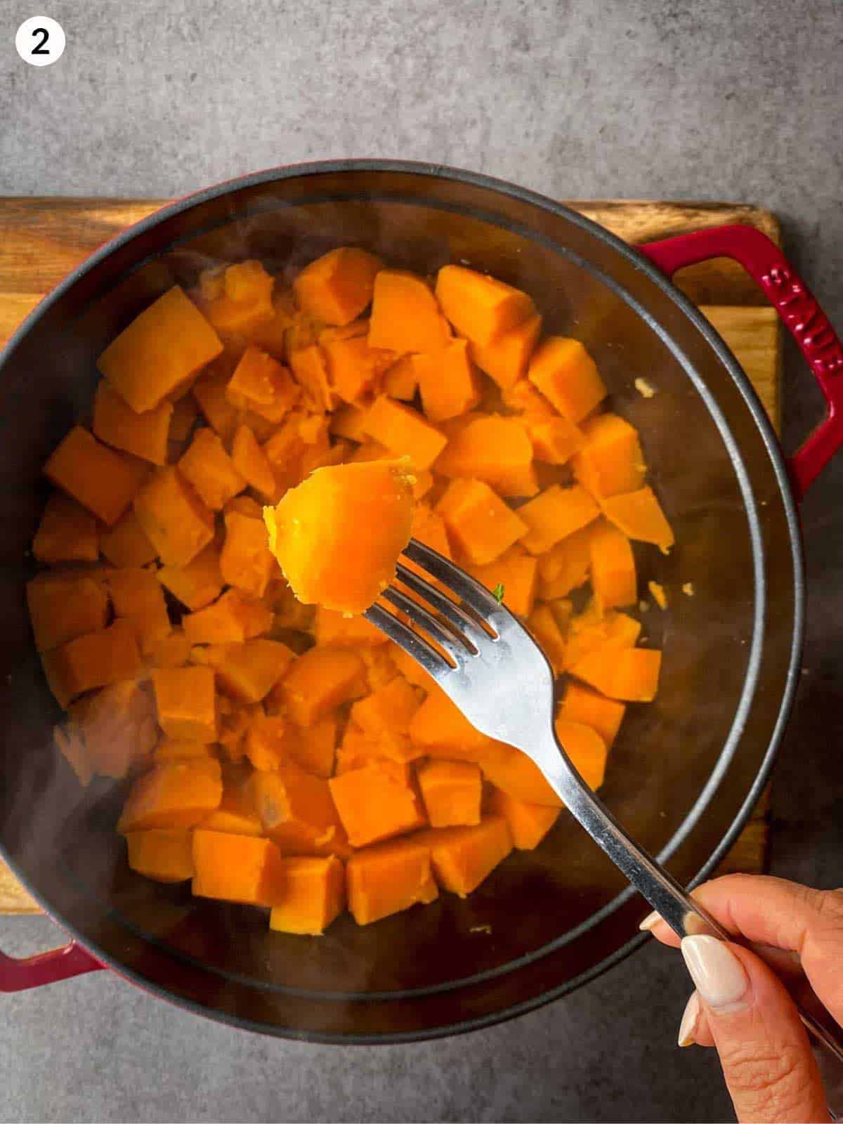 A fork lifting a cooked sweet potato cube from a Dutch oven