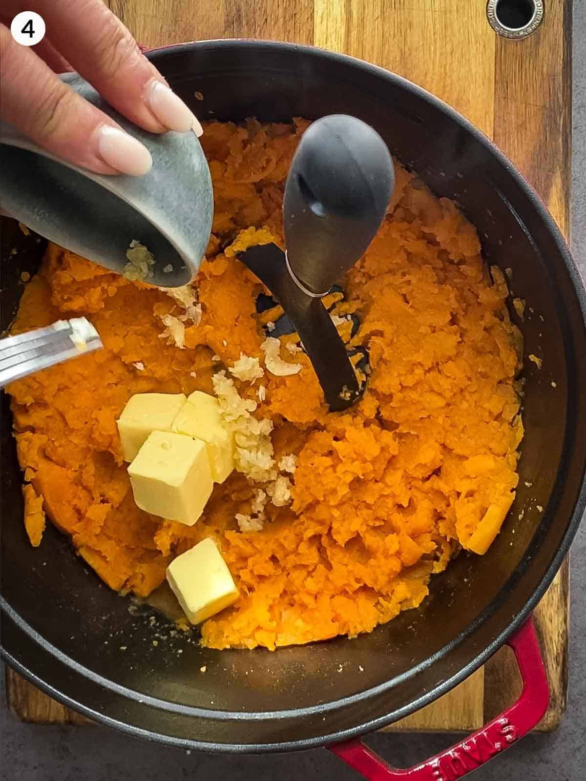 Adding butter into mashed sweet potato in a dutch oven sitting on a wooden board