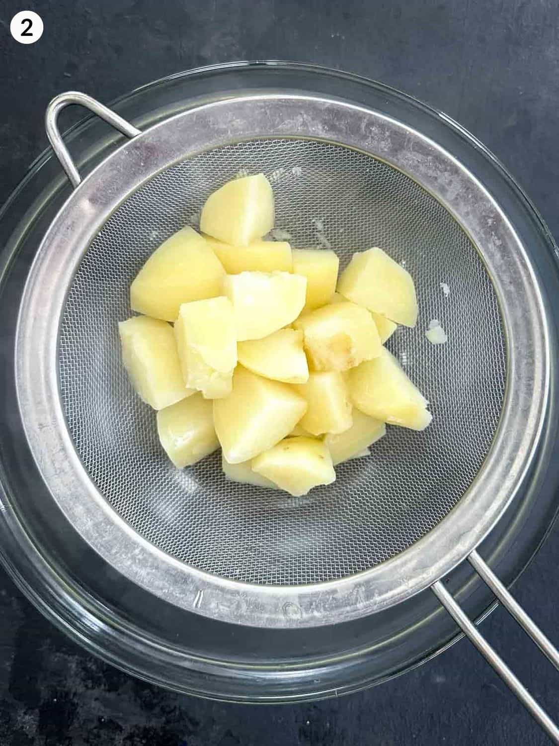 Straining cooked potatoes on a colander over a mixing bowl