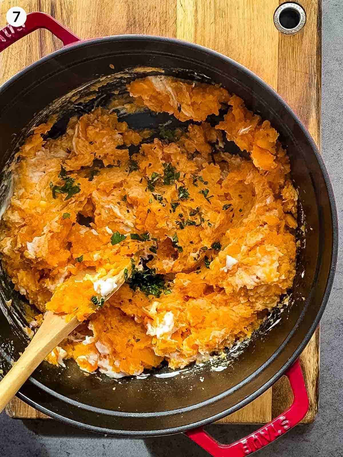 Mixing herbs into mashed sweet potato in a Dutch oven with a wooden spoon