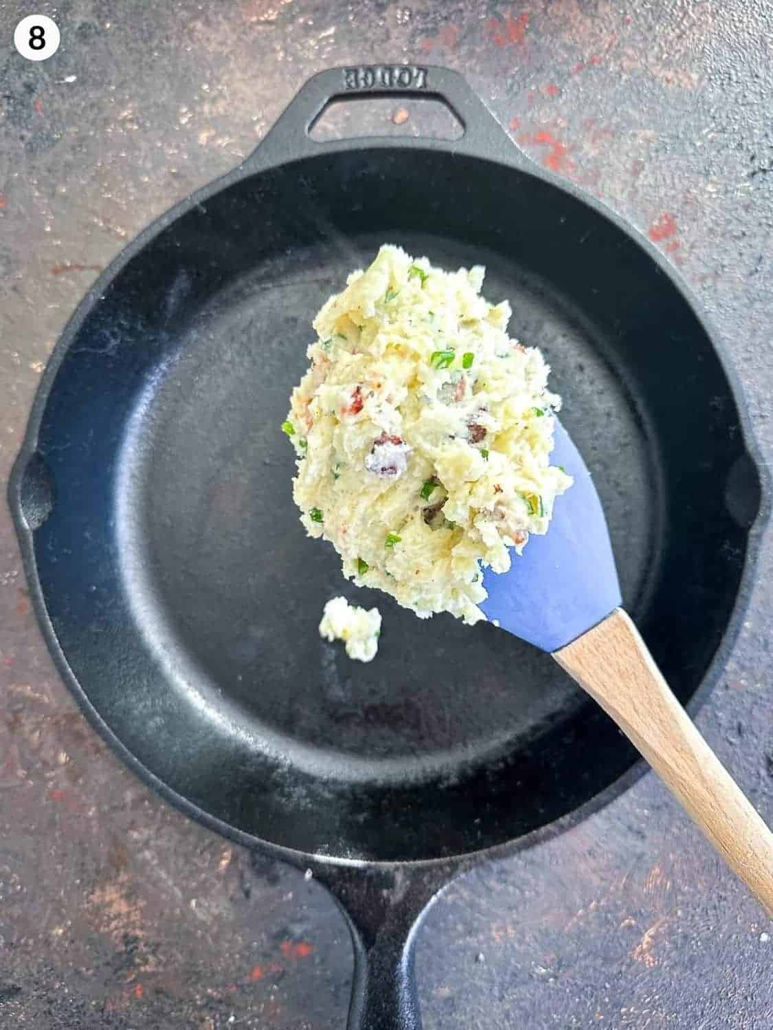 Adding loaded mashed potato onto a skillet with a blue spatula