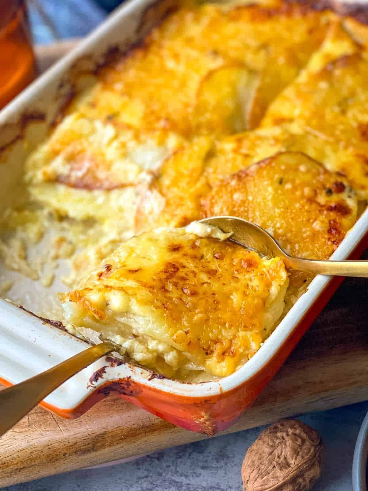 Lifting a serve of Creamy Potatoes au Gratin from a ceramic baking dish