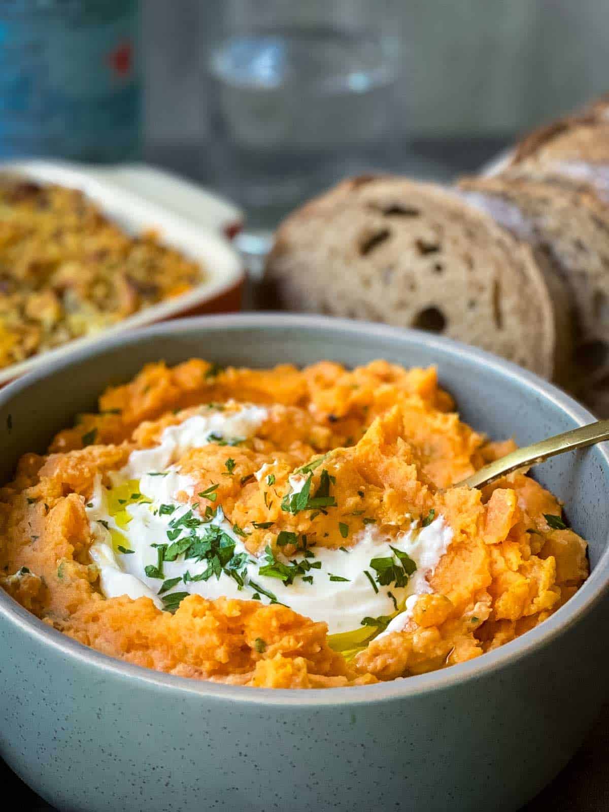 Bowl of mashed sweet potato in a grey bowl with a gold spoon served with bread on the side