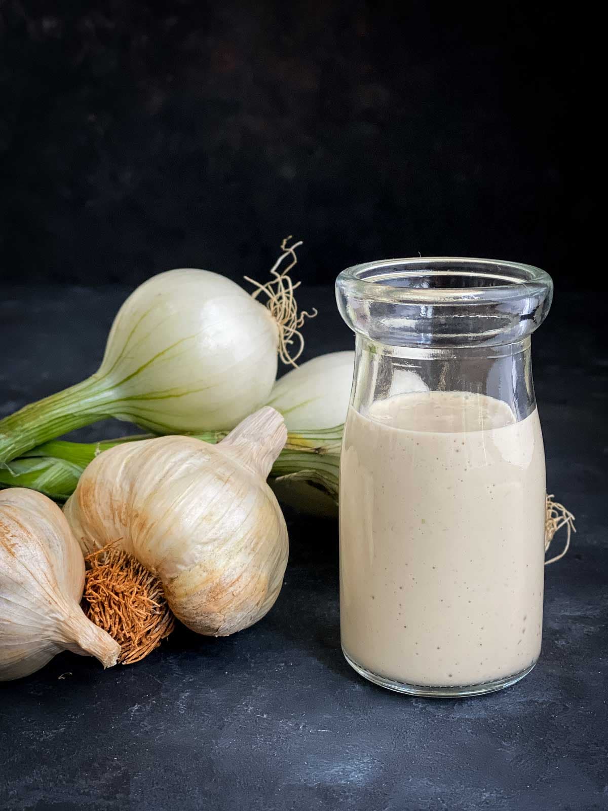 Creamy Garlic Dressing in a jar with whole garlic and salad onion on the side