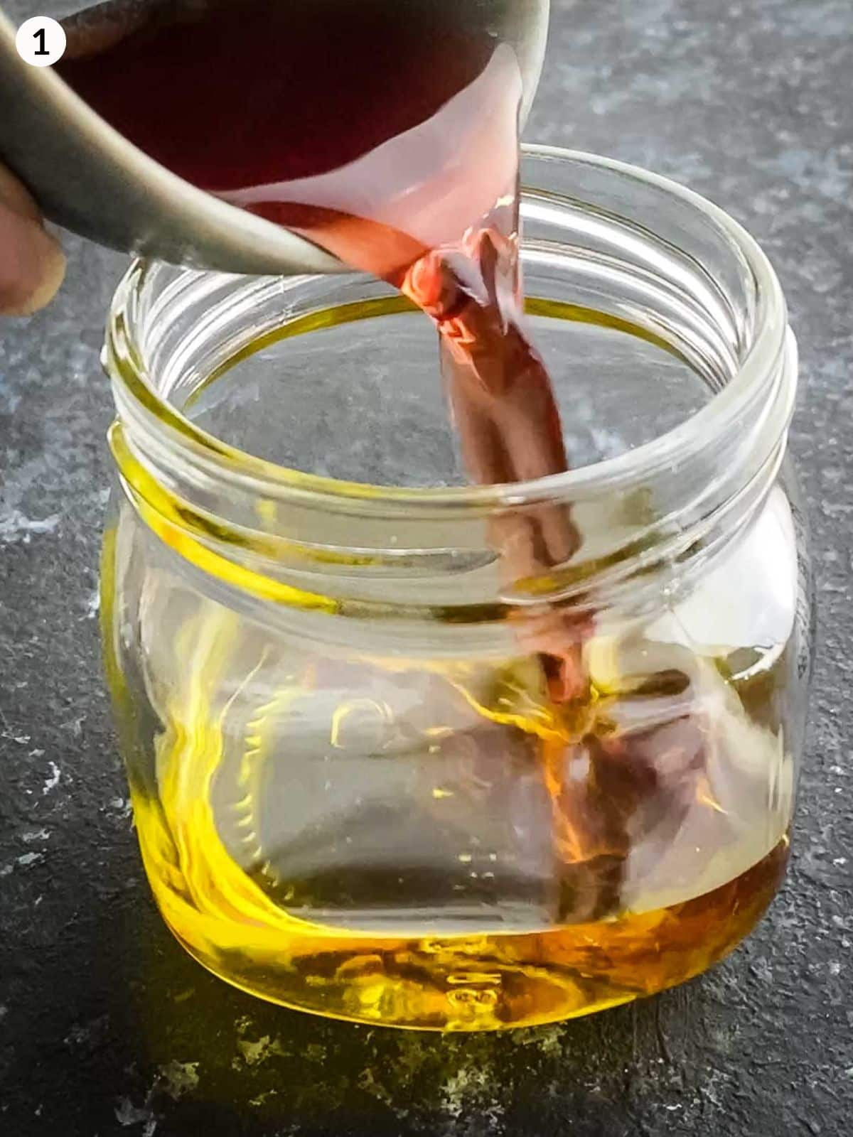 Pouring red wine vinegar into a jar of olive oil