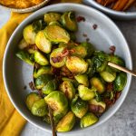 Brussels Sprouts With Bacon in a grey bowl with serving cutlery.