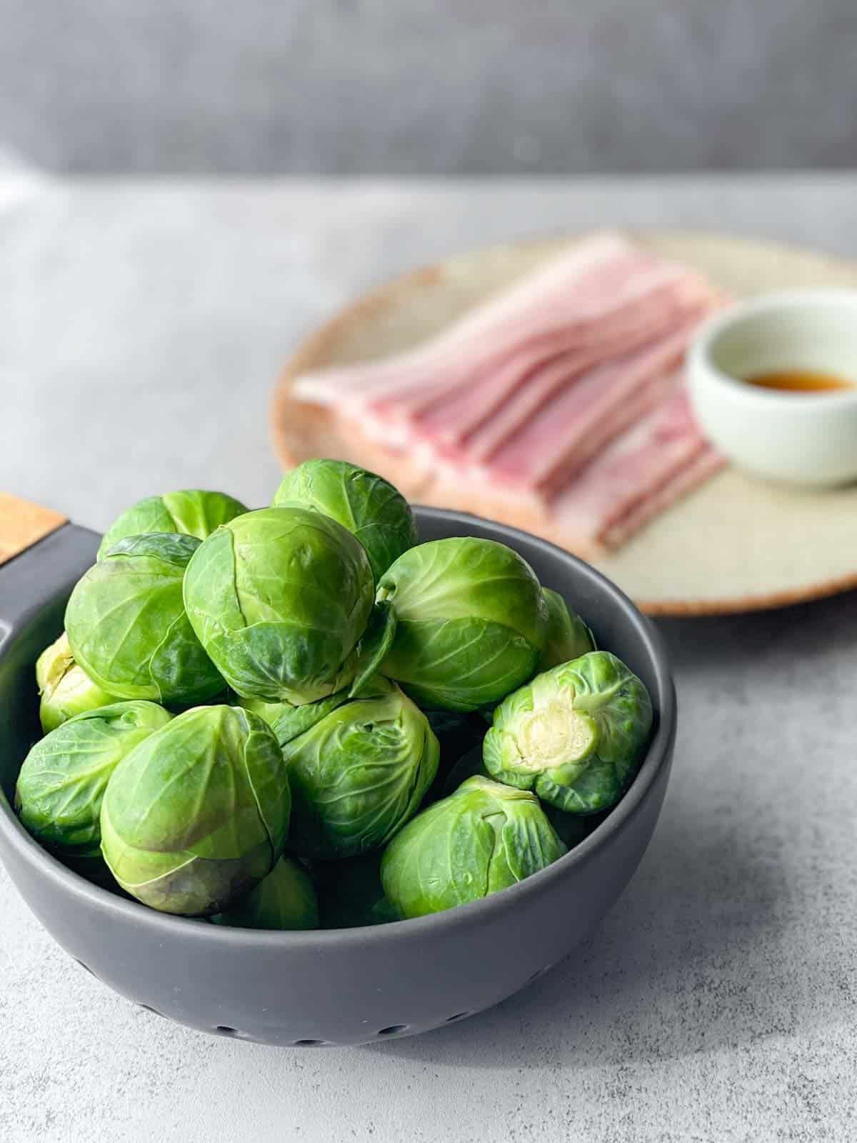 bowl of raw Brussels sprouts with bacon and maple syrup on a plate in the back ground