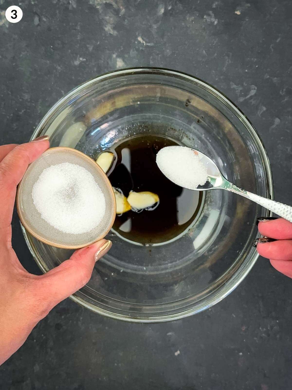 Adding sugar with a teaspoon with a salad dressing mixture in a clear bowl