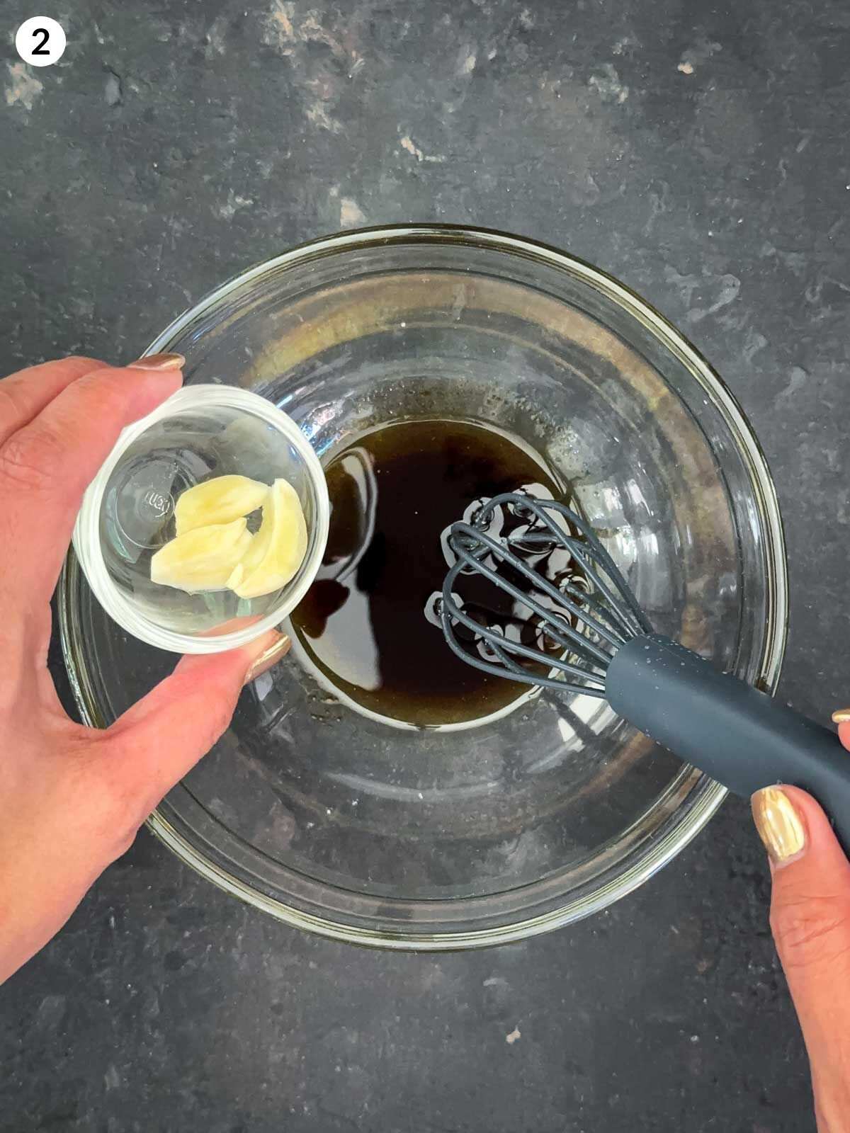 Whisking balsamic vinegar and olive oil in a bowl and adding cloves of fresh garlic