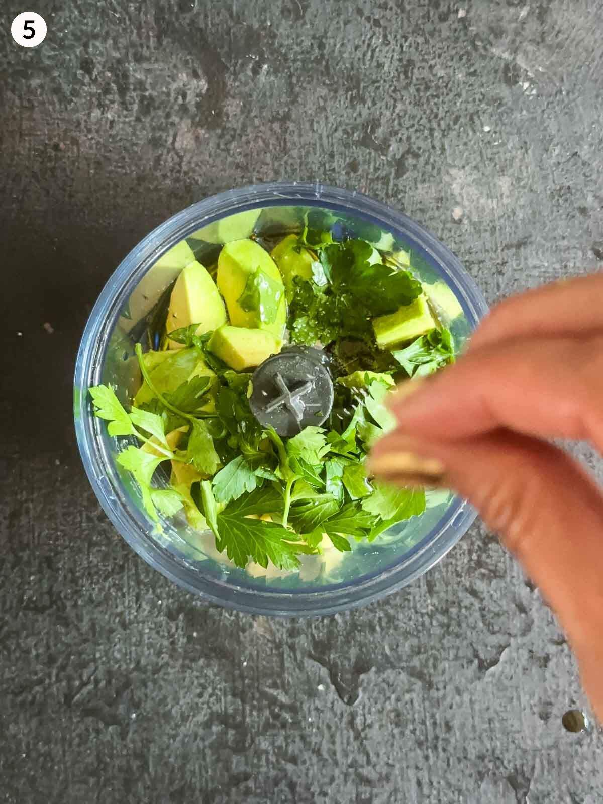 Adding salt into a food processor with chopped avocado and parsley