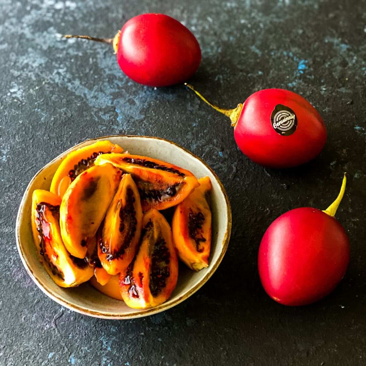 3 whole tree tomatoes next to a bowl of tree tomato wedges