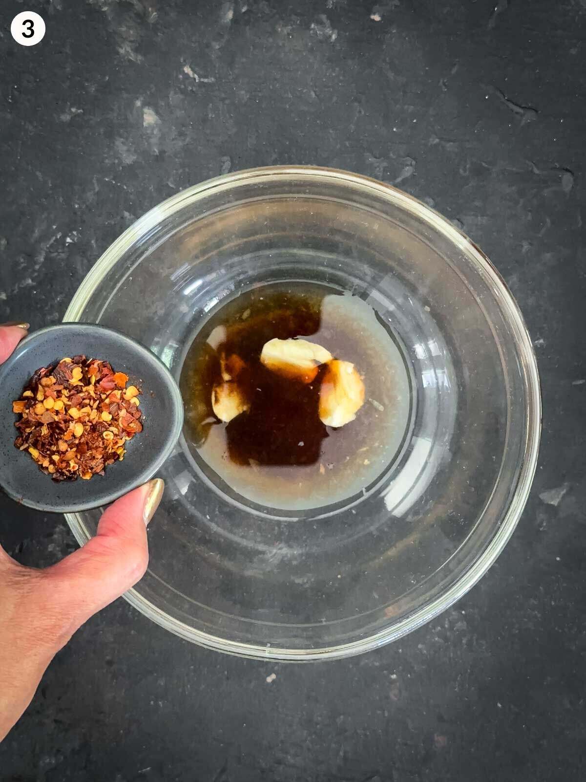 Adding chilli flakes to chilli soy dressing in a clear mixing bowl