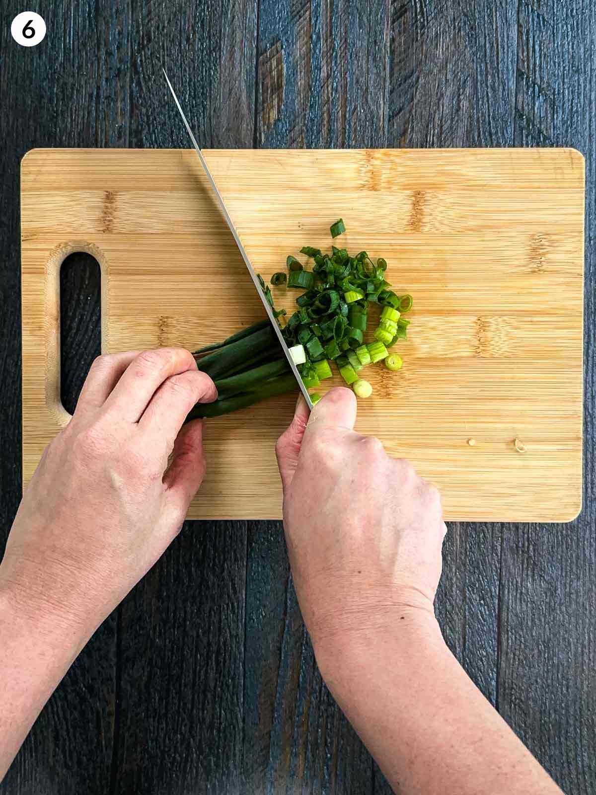 Cutting scallions on a wooden chopping board with a knife