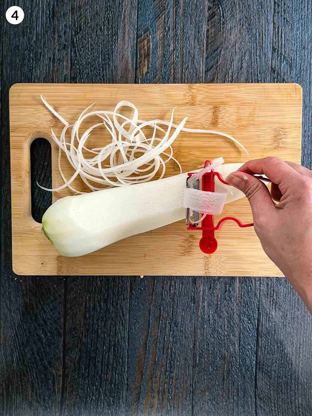 Shredding white radish with a shredding peeler on a wooden chopping board