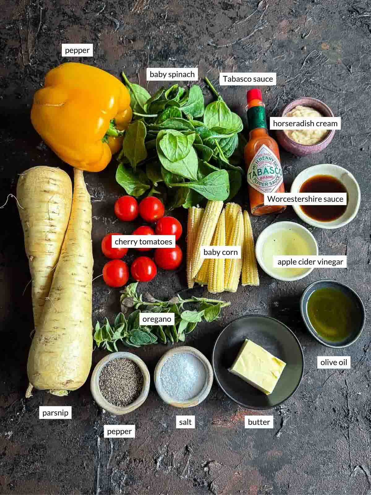 Flat lay of baby corn salad ingredients — parsnip, baby corn, baby spinach, cherry tomatoes, oregano, yellow capsicum, butter, olive oil, apple cider vinegar, Worcestershire sauce, Tabasco, and horseradish cream.